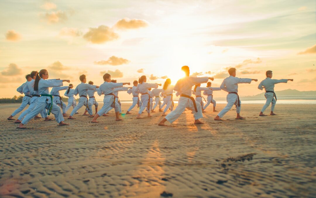 a group of people doing karate on a sandy beach at sunrise