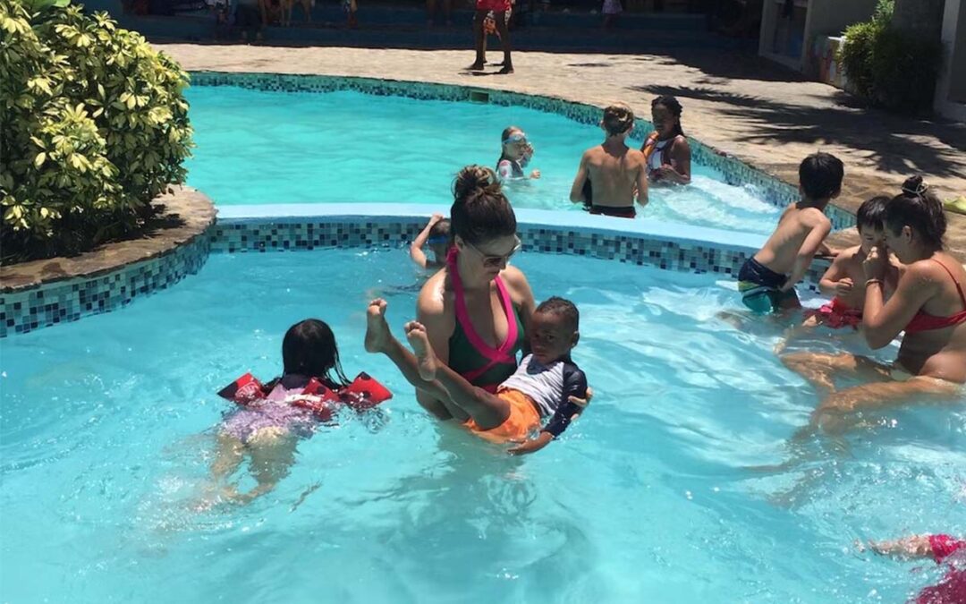 A woman stands in a swimming pool surrounded by young children learning to swim.
