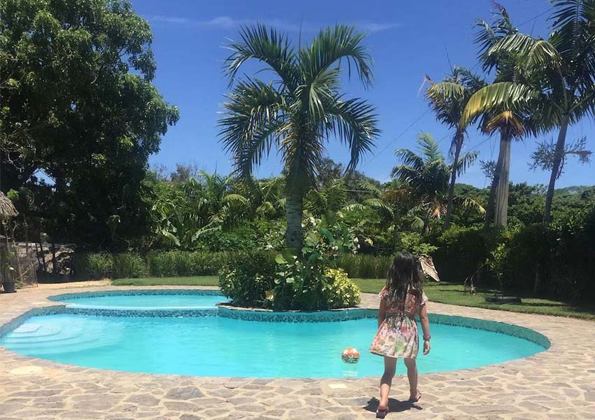 A young girl walking towards a swimming pool with a blue sky and palm trees in the distance