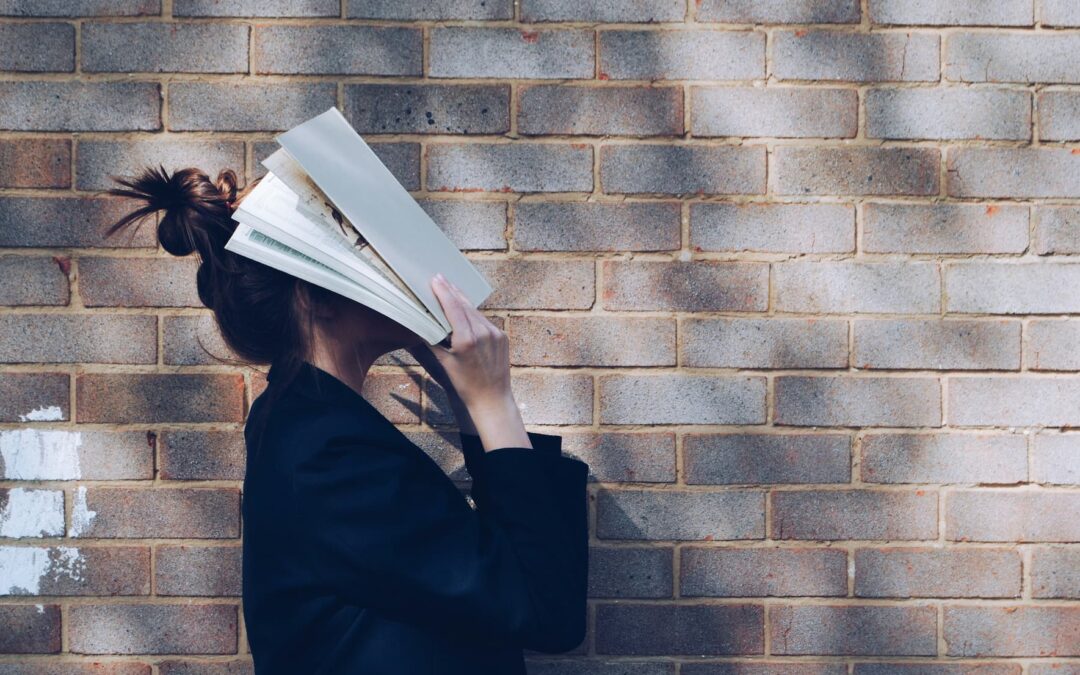 School girl holding book up to her face in front of natural rustic red brick background